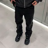 Pantalón de denim negro con acabado encerado, corte acampanado y diseño decorado con rombos formados por pedrería brillante en toda la superficie.