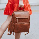 Mochila de símil cuero color marrón, con apertura superior, dos bolsillos frontales con cierre metálico y bolsillos laterales. Incluye tres bolsillos internos y correa extraíble.