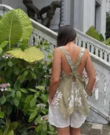 Top de lino blanco con bordado floral de gran tamaño en tonos cobrizos. Presenta un diseño de espalda descubierta con tirantes anchos cruzados y un bajo asimétrico y fluido.