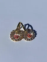 Aros colgantes con forma circular, con strass plateado alrededor y flor de vidrio amarilla con centro rojo en el interior. El arito es de acero quirúrgico.