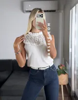 Blusa blanca sin mangas, de símil lino, con cuello alto y detalle de encaje calado y volados en el escote.