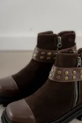 Bota corta de gamuza marrón con puntera de cuero liso, suela track negra y correa desmontable con tachas metálicas.