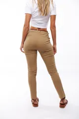 Pantalón de vestir color beige, de corte recto, con bolsillos laterales y traseros. Se ajusta a la cintura con cinturón de cuero marrón.
