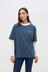 Remera de manga corta color azul, con calce clásico y tajos laterales. Presenta un bordado pequeño en el pecho con el texto 'UNIFORM STUDIO LAB' y un detalle bordado en la manga. Confeccionada en algodón lavado con textura suave.