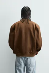 Cazadora bomber negra de corte regular fit, confeccionada en tejido efecto ante. Cuenta con cuello, puños y bajo en rib elástico, manga larga, bolsillos de vivo en la cadera y un bolsillo interior. Cierre frontal con cremallera.