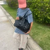 Bolso negro de cuero sintético con doble asa de hombro y correas decorativas frontales con hebillas metálicas. Incluye cierre superior y bolsillo interior.