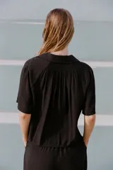 Camisa negra de cuello solapa con escote pico y manga corta. Detalle de nido de abeja en espalda. Cierre frontal con botones.