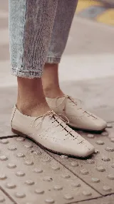 Zapato plano tipo Oxford de cuero color off white, con cordones finos frontales y punta cuadrada.