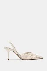 Zapato de tacón destalonado color beige, con cuerpo de tejido perforado, escote en pico, tira elástica trasera, tacón alto fino y acabado en punta.