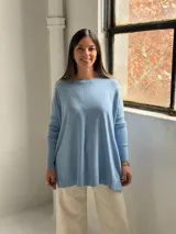 Sweater de punto color celeste, con cuello redondo, corte holgado y mangas largas con puños acanalados. Presenta un detalle de costura vertical central en el frente.