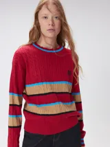 Sweater de punto cable color marrón con rayas horizontales en violeta y amarillo. Presenta cuello redondo acanalado, mangas largas con puños a juego y logo bordado en el pecho.
