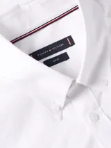 Camisa blanca de Tommy Hilfiger de corte slim fit, manga larga y cuello abotonado. Tiene el logo de la marca bordado en el pecho.