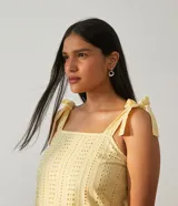 Vestido midi amarillo de algodón con tejido laise (ojales), escote cuadrado y tirantes ajustables con lazo. Presenta un diseño escalonado con volados en la falda.