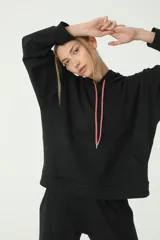 Buzo hoodie negro oversize de rústico, con capucha y cordones de ajuste color salmón y verde. Etiqueta con logo Basset 00'S en la manga derecha.