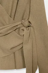 Chaqueta de punto de color tostado, con escote en V y manga larga. Diseño cruzado al frente con cinturón lazada en el mismo tejido y detalle de hebilla metálica circular en el lateral.