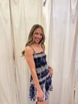 Vestido corto de tirantes finos con estampado tie-dye en tonos azul, negro y gris. Presenta un escote recto con frunce central y un volado en el ruedo de una textura diferente.