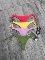 Bombacha de bikini tipo colaless con laterales regulables mediante lazos. Se presenta en cinco colores: naranja, negro, lila, amarillo flúor y blanco, y rojo.