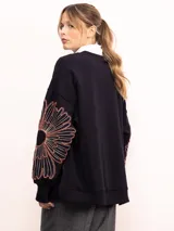 Buzo de algodón color negro con cuello redondo, mangas largas y bordado floral XL en color cobre en las mangas. Presenta un diseño holgado y cómodo.