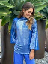 Blusa de manga larga color azul eléctrico con acabado brillante o metalizado, cuello alto y corte holgado.