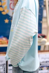 Polo de manga larga en color marrón con rayas horizontales azules en las mangas. Presenta cuello tipo polo en azul con detalles de rayas, cierre frontal parcial con botones y estampado frontal con la frase 'From Uruguay to the World'. Incluye un parche bordado en el pecho.