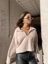 Buzo de cuello polo con escote en V, de corte holgado y diseño cropped. Presenta mangas largas con puños ajustados y una textura suave.