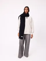 Bufanda de tejido de punto grueso en color negro, con etiqueta de la marca Rusty en uno de los extremos.