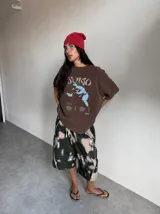 Remera marrón oversize con efecto acid wash, corte amplio y mangas cortas. Presenta un estampado frontal en tonos celestes y grises con la inscripción 'Sumo', una ilustración de un luchador de sumo y detalles tipográficos alusivos a un álbum musical.