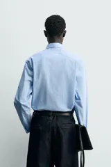 Camisa de algodón celeste con rayas verticales finas en blanco, de corte relajado (relaxed fit), cuello solapa y manga larga con puño abotonado.