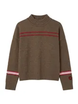Polera de lambswool color marrón, con cuello media polera, diseño de rayas horizontales en contraste en la parte superior delantera y en las mangas, y detalle de pin con logo en el puño.