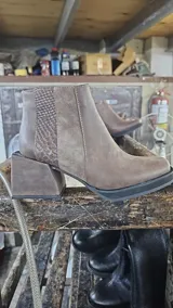 Bota corta de cuero vacuno color marrón, con diseño de paneles combinados en cuero liso y cuero texturizado tipo reptil en el talón. Presenta un taco cuadrado de madera forrado en cuero y suela de goma, con cierre lateral interno y punta cuadrada.