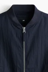 Campera bomber en mezcla de algodón y nylon color azul marino, con cuello elevado acanalado, cierre frontal, bolsillos laterales y un bolsillo con cierre en la manga.