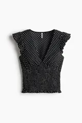 Top entallado en punto texturizado color negro con estampado de lunares blancos, escote en V, mangas cortas con volados y cuerpo fruncido tipo smock.