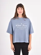 Remera de corte holgado y diseño oversize, color gris azulado con efecto lavado. Presenta un estampado gráfico central con tipografía y motivos florales.