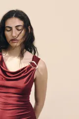 Vestido midi color vino tinto, sin mangas, con escote drapeado tipo cascada y un detalle de argolla metálica plateada en el bretel derecho. Presenta frunces laterales a lo largo del torso.