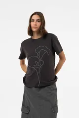 Remera de algodón con calce relajado, color negro lavado, cuello redondo y mangas cortas. Presenta una estampa floral bordada en líneas blancas en el frente.