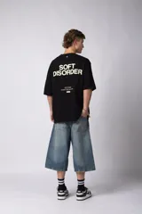 Remera de corte oversize color negro, confeccionada en algodón premium. Presenta un diseño gráfico minimalista estampado en el frente con tipografía y logotipos en color crema.