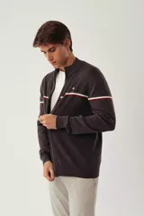 Campera tejida color verde militar, con cuello alto, cierre frontal completo, logo bordado en el pecho y rayas horizontales en blanco, marrón y azul marino.