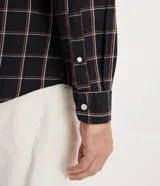 Camisa de hombre de manga larga, confeccionada en franela ligera con estampado cuadrillé en tonos oscuros y líneas finas blancas y naranjas. Cuenta con cuello clásico y abotonado frontal.
