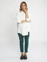 Camisa blanca de corte oversize, con cuello clásico, cierre frontal con cartera oculta y bolsillo delantero. Presenta mangas largas con puños abotonados.