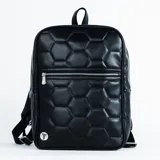 Mochila negra con diseño acolchado de hexágonos que simula la textura de una pelota de fútbol. Cuenta con un bolsillo frontal con cierre metálico y logo circular plateado en la parte inferior.
