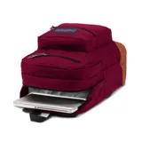 Mochila Jansport color borgoña con base de cuero sintético marrón. Tiene dos compartimentos principales, funda interna para laptop, bolsillo lateral para botellas, bolsillo frontal con panel de organización y clip para llaves, panel trasero acolchado, dos bolsillos exteriores con cremallera y tirantes ergonómicos curvados en S.