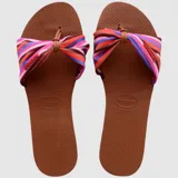 Sandalias tipo ojota Havaianas con base de goma color marrón y tira frontal de tela anudada con estampado de rayas multicolor en tonos rosados, violetas, naranjas y marrones.