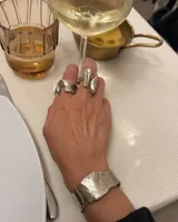 Anillo de diseño orgánico y macizo con forma irregular, elaborado en metal con acabado brillante. Presenta una estructura abierta que permite su ajuste.