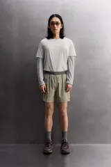 Pantalón corto de trail running color beige, confeccionado en tejidos técnicos ligeros y elásticos. Cuenta con forro interior, cintura elástica ajustable con cordón, bolsillos traseros laterales multifunción, bolsillo trasero central con cremallera, bajo con costura termofijada y aberturas laterales. Incluye logo estampado en la pernera.