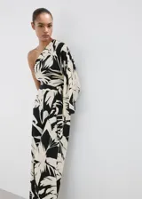 Mono largo de viscosa con diseño bicolor en negro y beige con estampado de hojas tropicales. Presenta un corte asimétrico de un solo hombro con manga larga holgada, pantalón de silueta recta y lazo ajustable en la cintura.