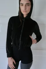 Campera negra de terciopelo con capucha, cierre frontal y bolsillos laterales.