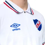 Remera polo azul marino con cuello clásico y puños con detalles tricolor (blanco, rojo y azul). Presenta logo de la marca Umbro bordado en blanco y escudo del Club Nacional de Football bordado en el pecho. Fabricada en tejido suave y respirable.