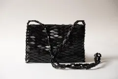 Cartera bandolera rectangular de diseño estructural, hecha completamente a mano en color negro, con textura de piezas superpuestas y correa larga elaborada con cuentas.