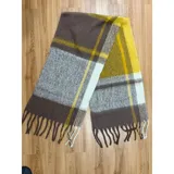 Bufanda rectangular de tejido grueso con diseño de cuadros en tonos azul, naranja, gris y beige, terminada con flecos en los extremos.