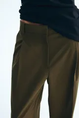 Pantalón verde militar de corte holgado, con pinzas delanteras, bolsillos laterales, bolsillos traseros decorativos y piernas amplias con pliegues marcados. Cuenta con cierre de botón y corchetes ocultos.
